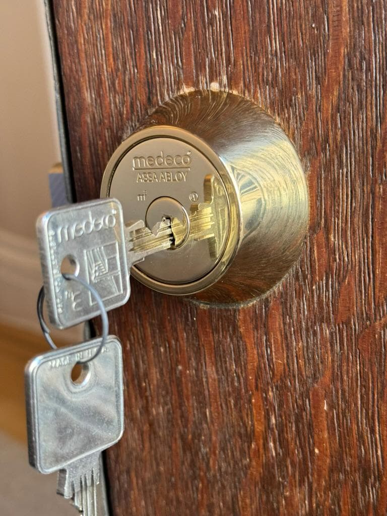 Brass Medeco deadbolt with two keys in the cylinder on a wood door