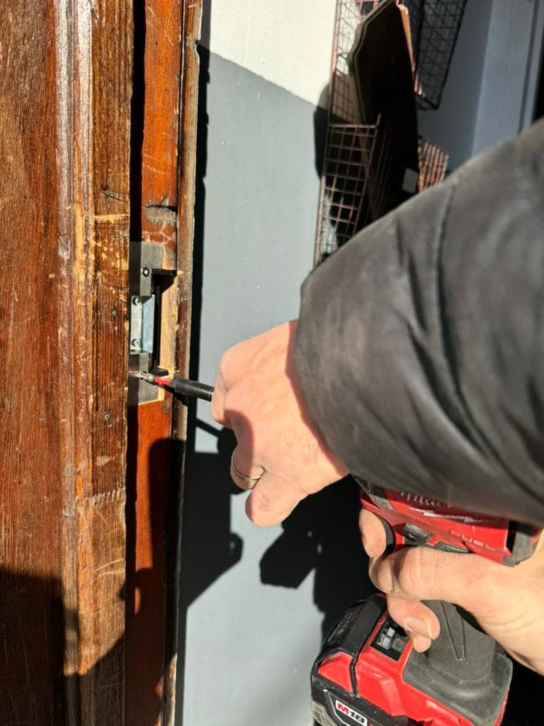 Hand driving a screw into the strike plate on an old wooden door frame with a cordless drill